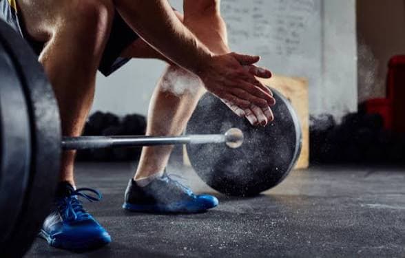 A lifter clapping chalk over a loaded barbell