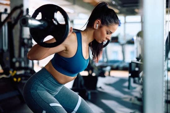 A member back-squatting a barbell on the gym floor